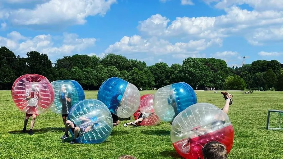 People playing bubble soccer on a grassy field.