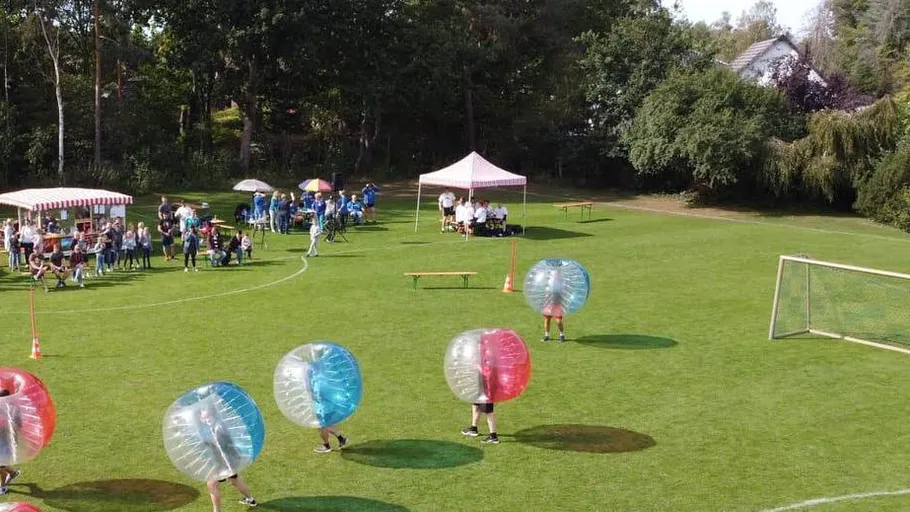 People playing bubble soccer on grassy field.