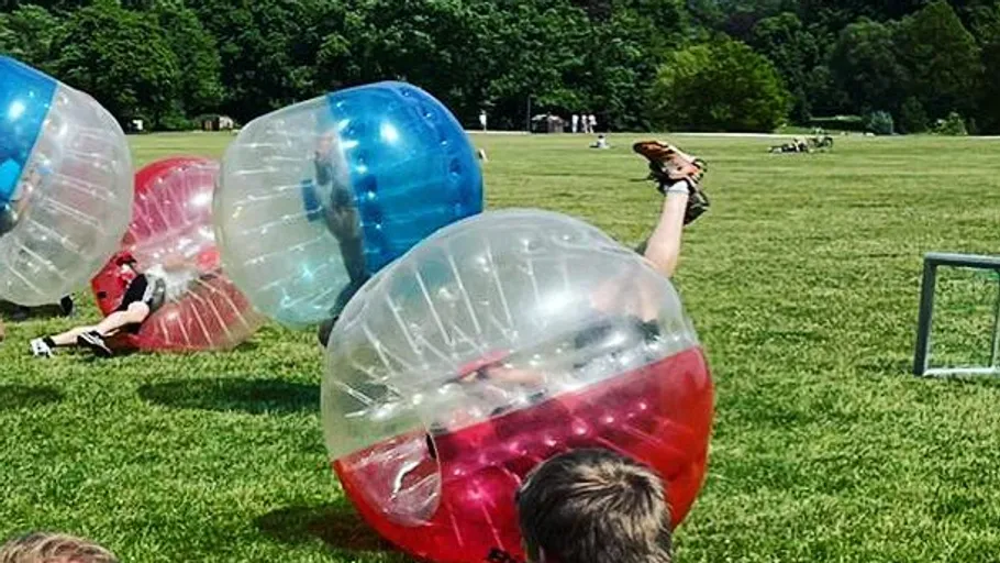 Personen spielen Bubble-Fußball in einem grünen Park.