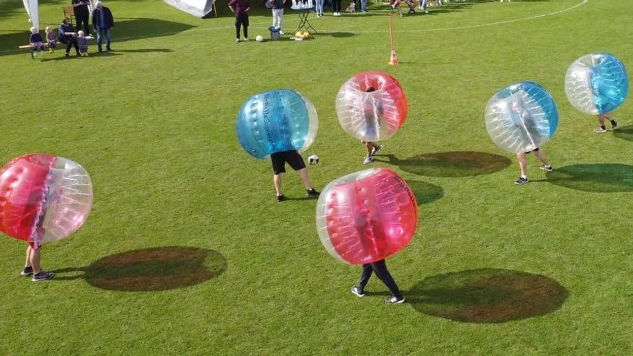 People in bubble suits playing soccer outdoors.