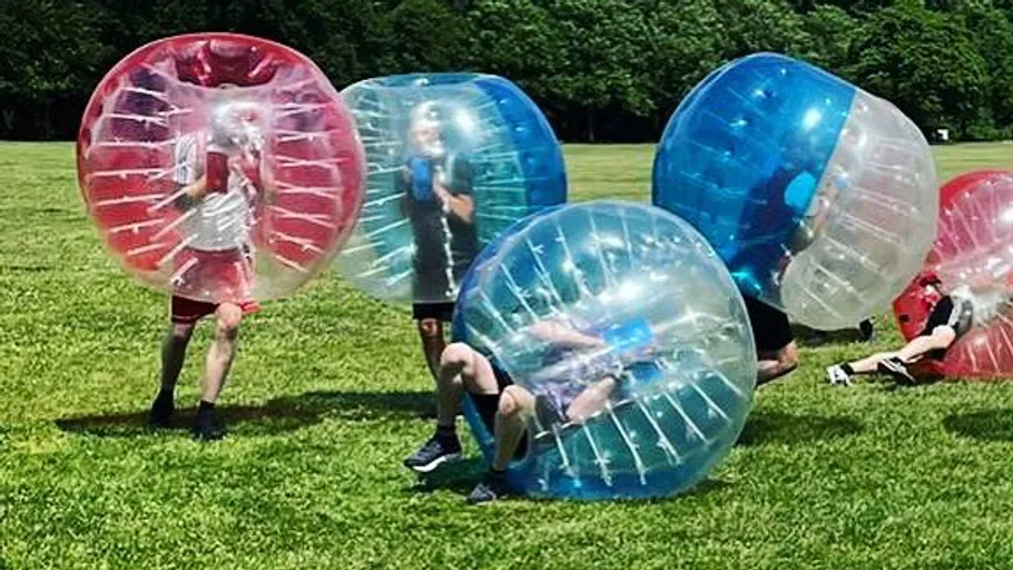People playing bubble soccer on grass field.