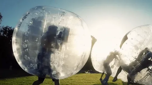 Personen spielen Bubble Soccer im Freien bei Sonnenuntergang.