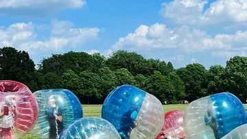 Personen in aufblasbaren Kugeln auf Wiese.