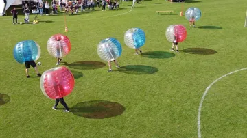 Leute spielen Bubble-Soccer auf Rasenfeld.