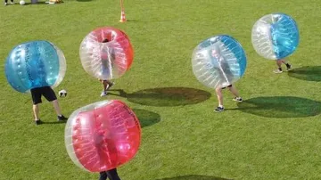 Personen spielen Bubble-Soccer auf Grasfeld.