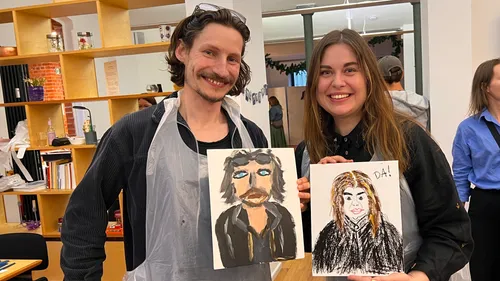 Two people smiling and holding painted portraits.