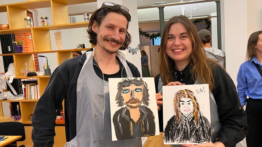 Two people smiling and holding painted portraits.