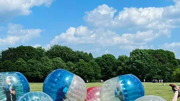 Menschen spielen in riesigen Bällen auf Wiese.