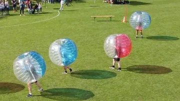 Personen spielen Bubble-Fußball auf Rasenfeld.
