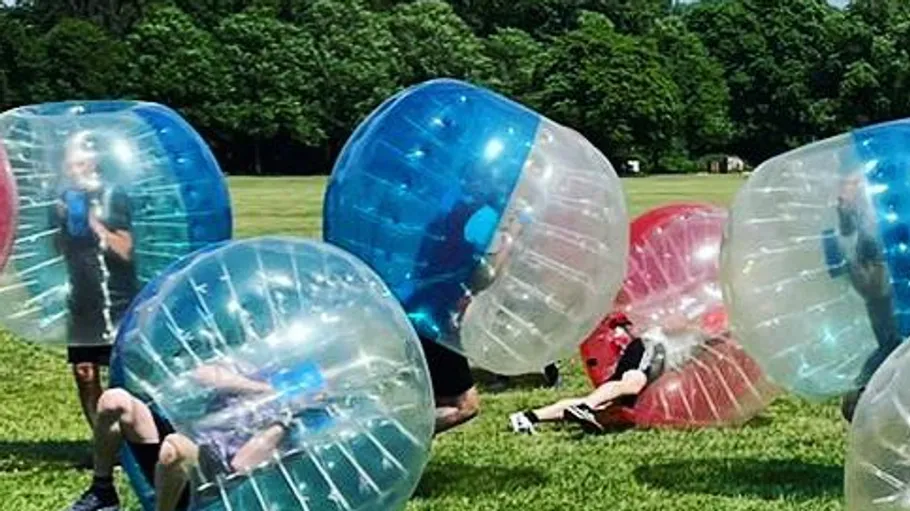 People inside inflatable bubbles on grass field.
