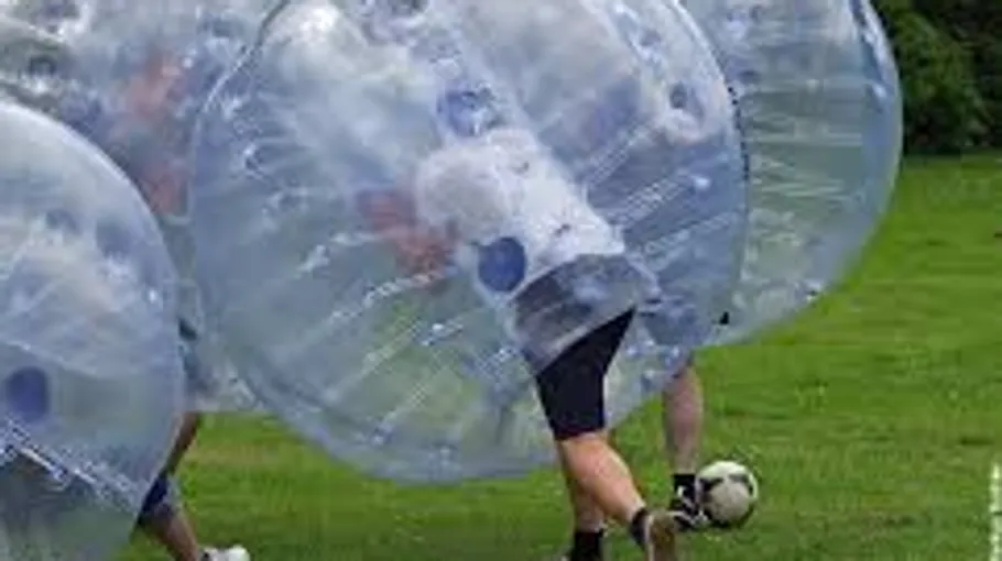 People playing bubble soccer on grass.