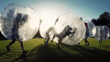 Menschen spielen Bubble-Fußball draußen im Sonnenlicht.