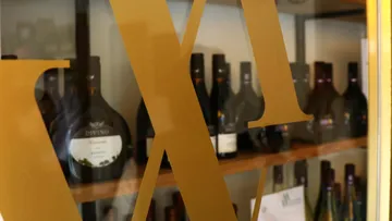Wine bottles seen through large gold letters.