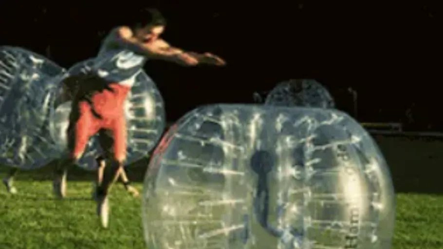 Person diving into inflatable bubble ball outdoors.