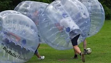 Personen in Bubble-Anzügen spielen Fußball im Freien.