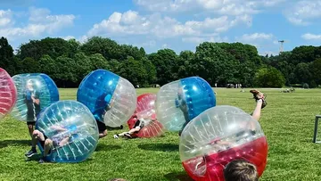 Menschen spielen Bubble-Fußball auf einer Wiese.