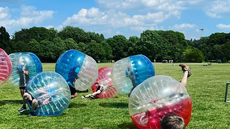 People playing bubble soccer in a field.