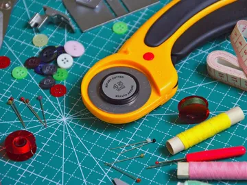 A rotary cutter and sewing supplies on a work mat.
