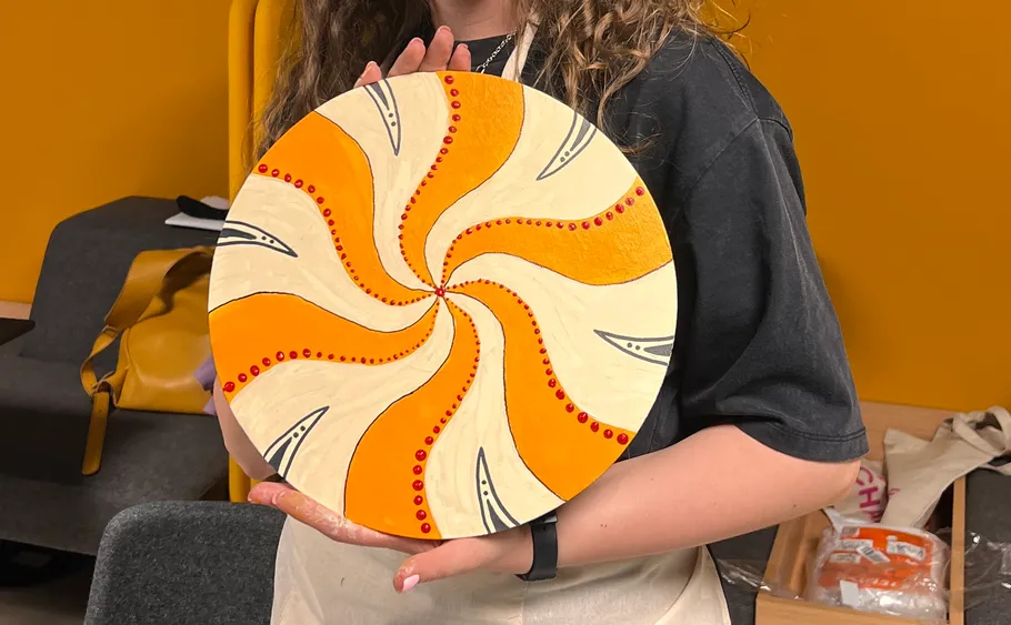 Person holding colorful circular artwork indoors.