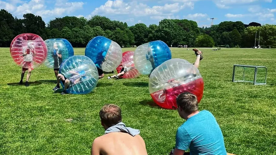 Personen spielen Bubble-Fußball auf Rasenfläche.