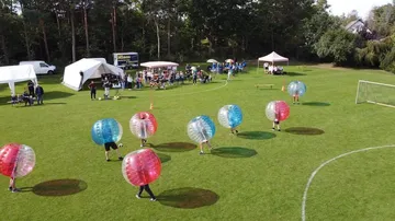 People playing bubble soccer on grassy field.