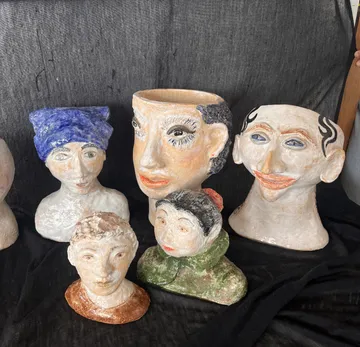 Tonskulpturen von menschlichen Gesichtern auf schwarzem Stoff.