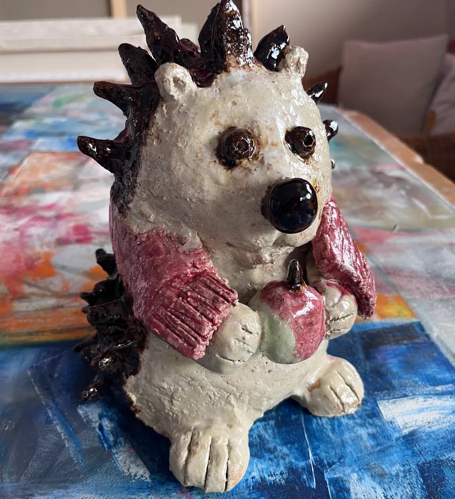 Ceramic hedgehog holding apple on colorful table.
