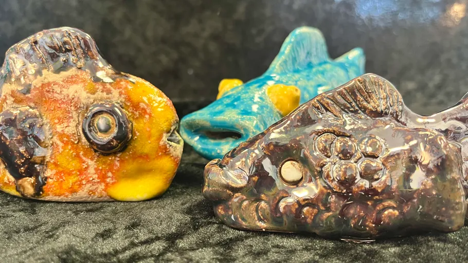 Drei Keramikfischskulpturen auf dunklem Stoff.