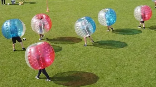 People playing bubble football on a grassy field.