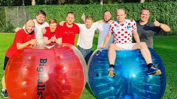 Men posing on inflatable balls outdoors.