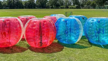 Inflatable bubble soccer balls on grassy field.