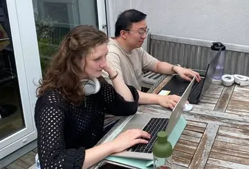 Two people working on laptops outside.