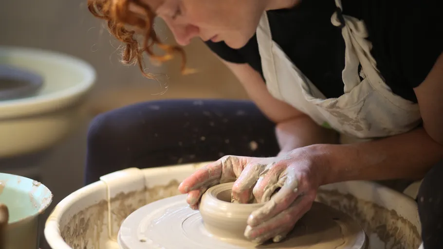 Person shaping clay on pottery wheel indoors.