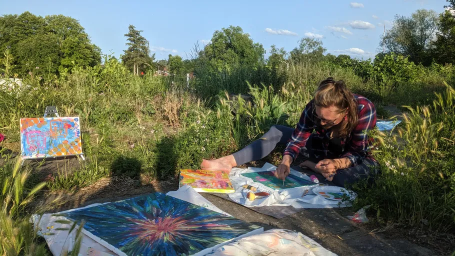 Person malt abstrakte Kunst im Freien, umgeben von Natur.