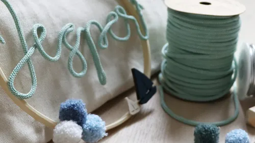 Garn "Jesper" auf Stoff mit Pompons.