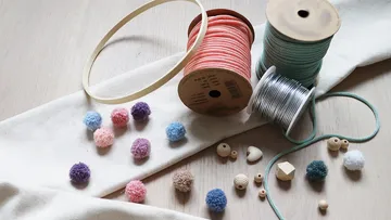Craft supplies on table including pom-poms and cords.