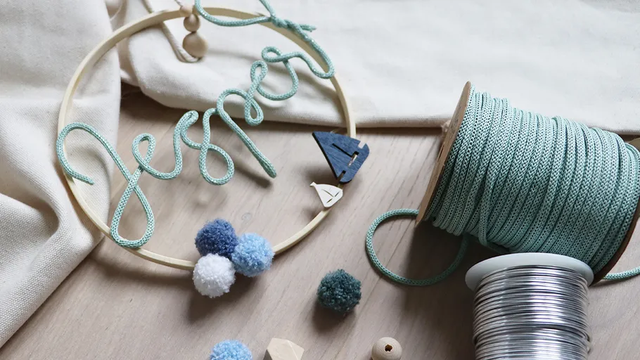 Decorative wire name with pom-poms on wooden surface.