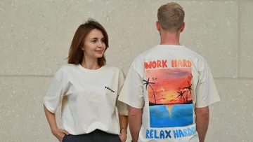 Zwei Personen tragen bedruckte T-Shirts, beige Wand.
