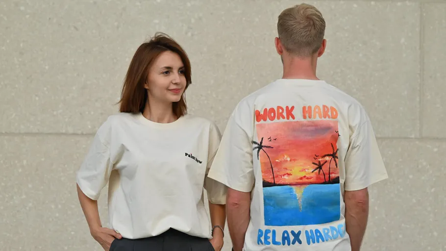 Zwei Personen tragen bedruckte T-Shirts, beige Wand.