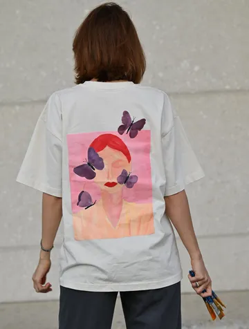 Person with butterfly t-shirt holding paintbrushes.