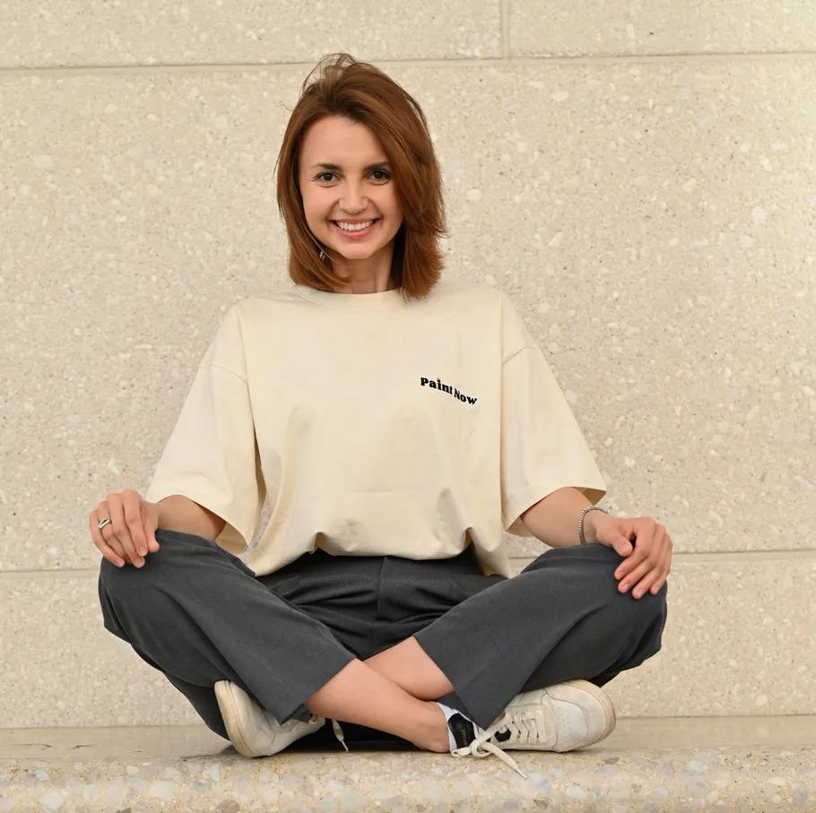 Woman sitting cross-legged, smiling against wall.