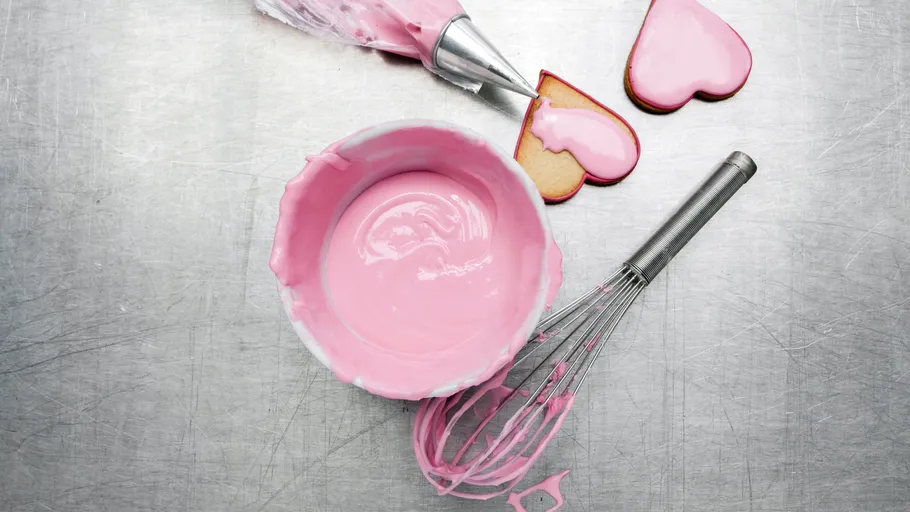 Schüssel mit rosa Zuckerguss, Schneebesen, Kekse.