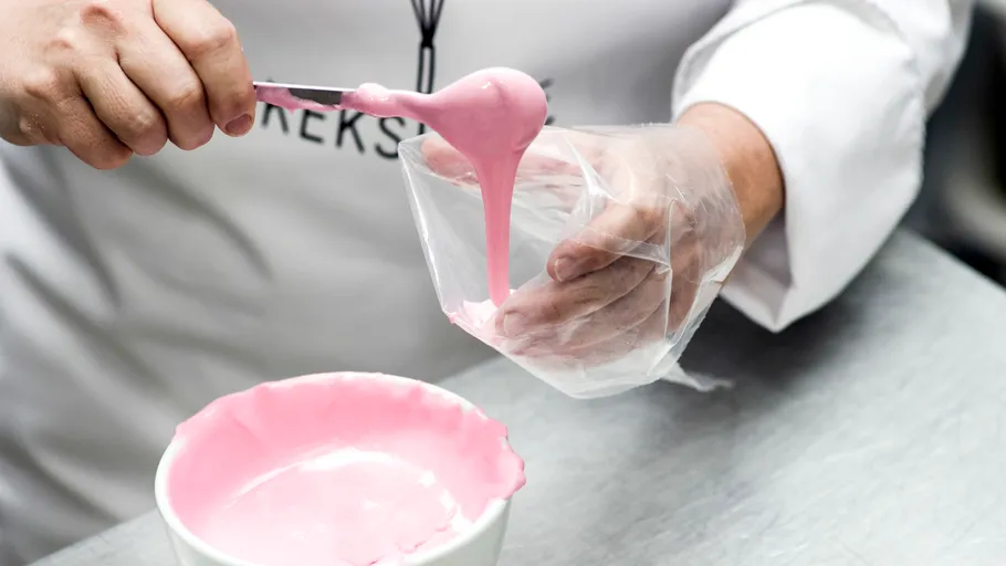 Person füllt Beutel mit pinkem Zuckerguss in Küche.
