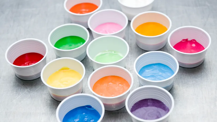 Bunter Teig in Plastikbechern auf Metalloberfläche.