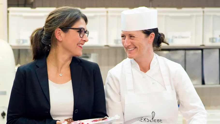 Two women smiling in a bakery environment.