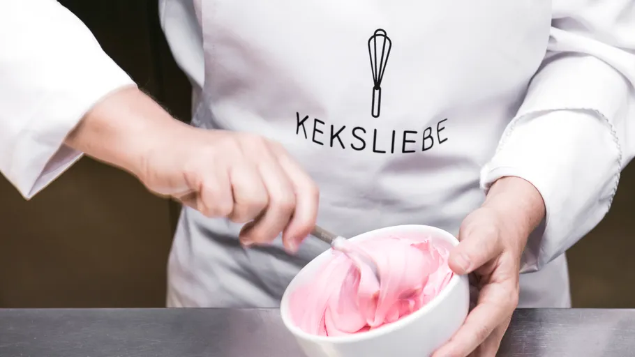 Person mischt rosa Zuckerguss in Schüssel.