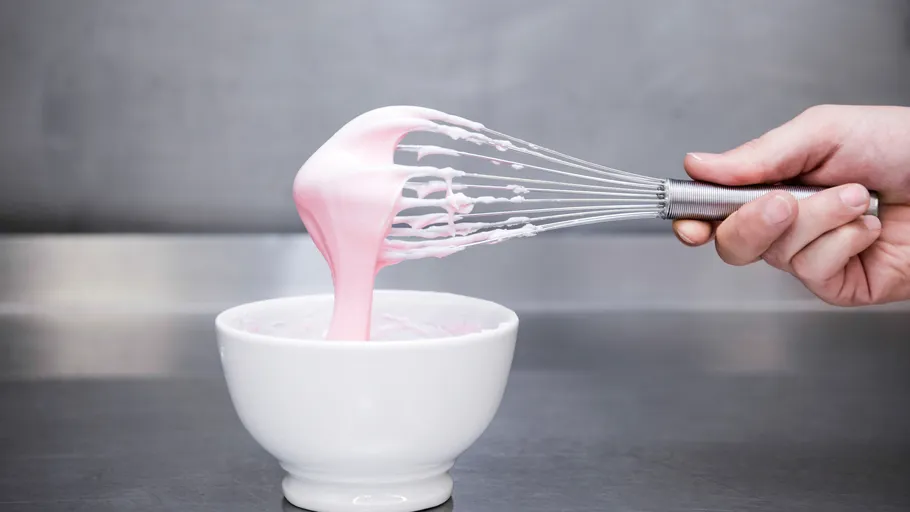 Hand schlägt rosa Zuckerguss in weißer Schüssel.