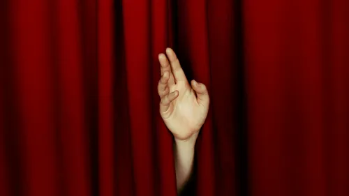 Hand reaching through red curtains.