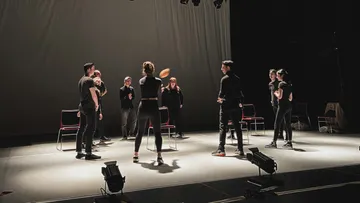 People in black rehearse with a ball on stage.