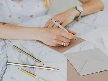 Hands write with pen on paper surrounded by envelopes.